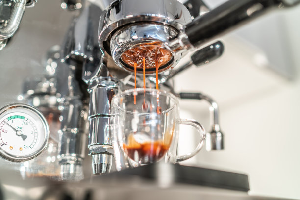 在家里的厨房里，一台咖啡机在无底过滤器里煮浓咖啡。美丽的奶油倒入透明的双层玻璃。图片下载