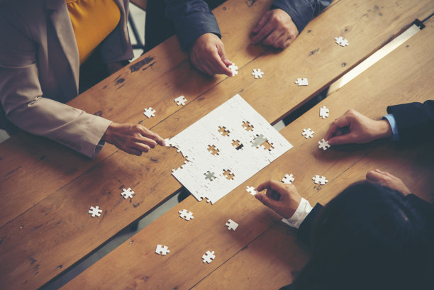在办公室开会的时候，一群商务人士手握着桌子上的七巧板，一起拼拼图。集合，解决方案，成功和战略概念。经营理念图片下载