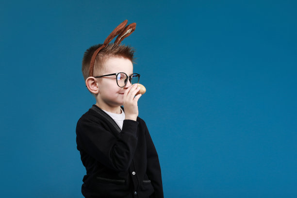 复活节快乐的孩子。男孩在兔子兔耳朵头上的颜色鸡蛋在蓝色的背景。戴眼镜的孩子笑容可掬图片下载