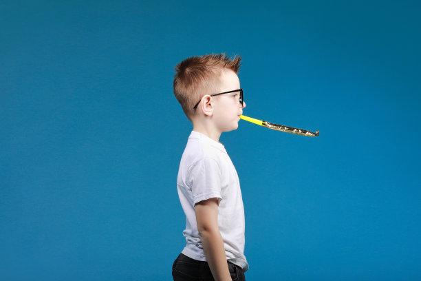 7岁的小男孩兴高采烈地戴着眼镜，在生日聚会上吹着节日的烟斗。儿童工作室肖像。童年的生活概念图片下载