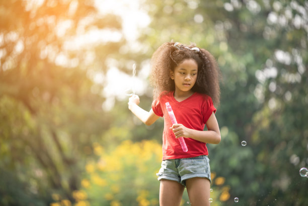小美籍非洲女孩在日落时分在户外吹肥皂泡图片下载