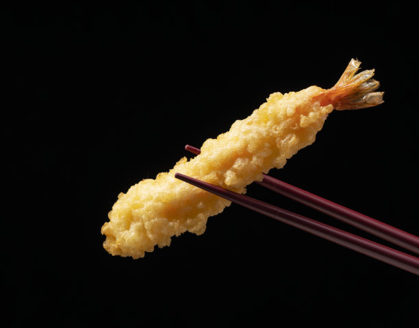 用筷子夹起虾天妇罗，背景是黑色的。图片下载