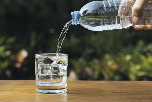 在自然背景下，将水倒入木桌上的玻璃杯中。图片下载