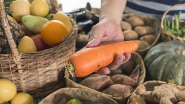 一名男子递上一根更大的胡萝卜出售。在一个小摊上买新鲜蔬菜。图片下载