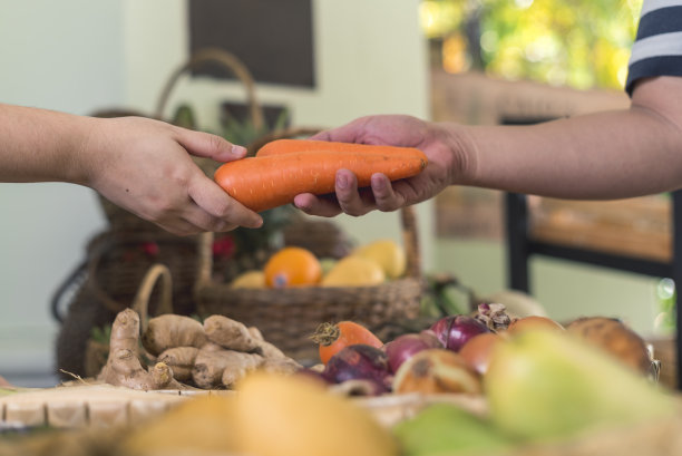 一个顾客递给一个小贩两块胡萝卜。在一个小市场的货摊上购买。图片下载
