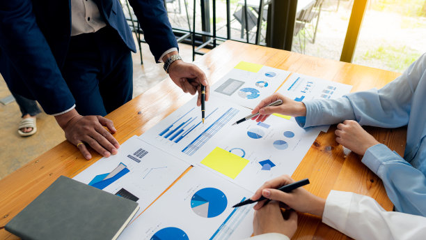 一群商人开会分析财务图表数据，为商业会计计划出谋划策。在办公室的桌子上放一个笔记本电脑和一个计算器。图片下载