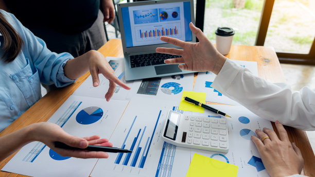 一群商人开会分析财务图表数据，为商业会计计划出谋划策。在办公室的桌子上放一个笔记本电脑和一个计算器。图片下载