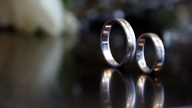 两枚金婚戒和白色背景上的玫瑰花。水平框中的图片。两枚结婚戒指和一张结婚请柬图片下载