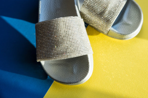 特写女孩或妇女的橡胶魅力时尚拖鞋站在蓝黄色的背景。银触发器滑块。度假旅游理念。Copyspace图片下载