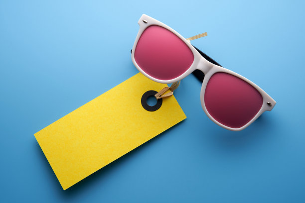 白色框架太阳镜与粉红色色调与黄色价格标签在蓝色的背景图片下载