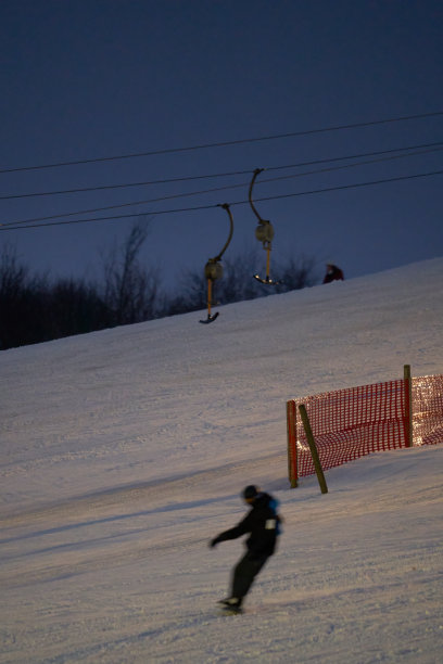 夜间有照明的滑雪牵引升降机在运行。冬季运动员在雪坡上。滑雪运动模糊。图片下载