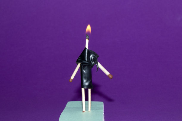 木制火柴和黑色丝带的创意概念，让时装模特用木制火柴棒穿黑色连衣裙，在紫色背景的发型上燃烧图片下载