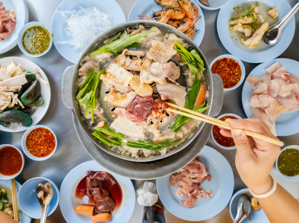 用木筷子夹着烤肉，泰式烤肉在热锅上烧烤，在热炉子上烤猪肉，一个假日家庭在餐馆吃饭。智能手机的照片图片下载