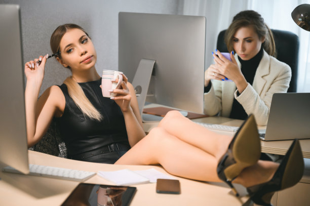 一名年轻女子把脚放在办公室的桌子上。两个女商人在一个共同工作的空间，在工作日或一周的结束，等待一个聚会图片下载