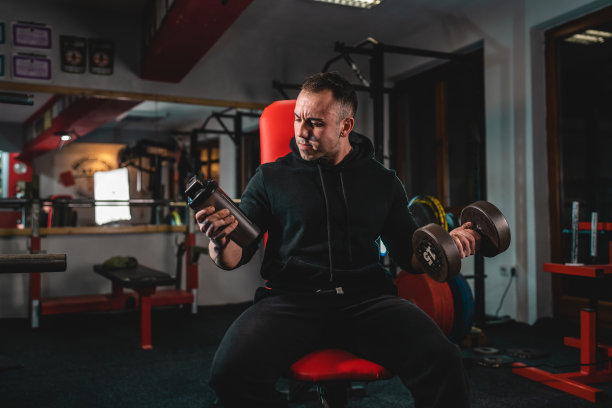 一名男子年轻的成年白人男性健美运动员训练手臂二头肌收缩肌肉与哑铃和补充摇壶而坐在健身房穿着衬衫黑暗照片真实的人复制空间前视图图片下载