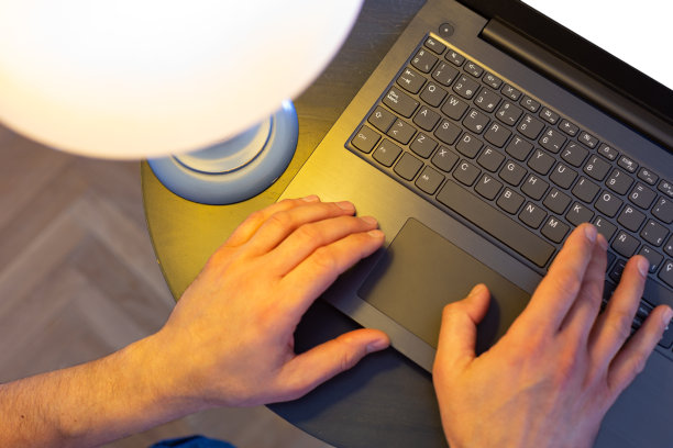 男性的手在被电灯照亮的笔记本电脑键盘上图片下载