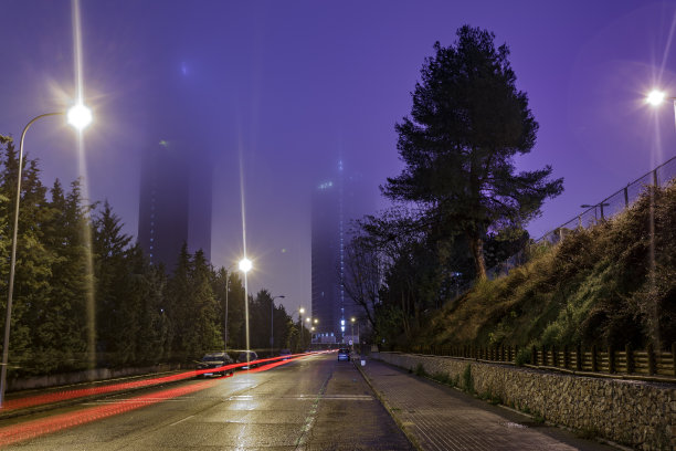 长时间暴露在雨夜雾天的街道上，树木林立，车辆稀少，摩天大楼在雾中。图片下载