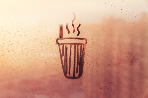 用吸管和蒸汽在日落的雾蒙蒙的玻璃窗上涂鸦一杯茶或咖啡图片下载