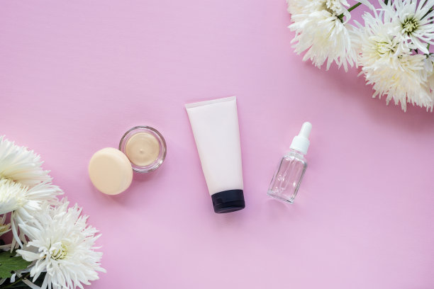 粉底在一个罐子，奶油管和玻璃瓶血清在粉红色的背景与菊花。美，化妆的概念。俯视图，平躺图片下载