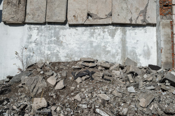 倒塌建筑的墙壁，在悬挂的混凝土板和一堆灰色的混凝土碎片之间有一个空间，还有干燥的植被。背景图片下载