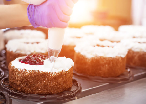 糕点师女孩用新鲜的饼干浆果和奶油做了一个蛋糕。批量生产糕点及糖果、糖果、奶油蛋糕装饰、工业图片下载