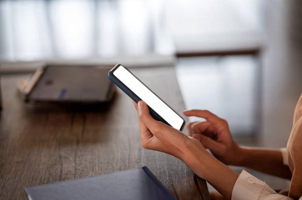 一个女商人的手坐在椅子上用智能手机的空白屏幕在咖啡。模拟。图片下载