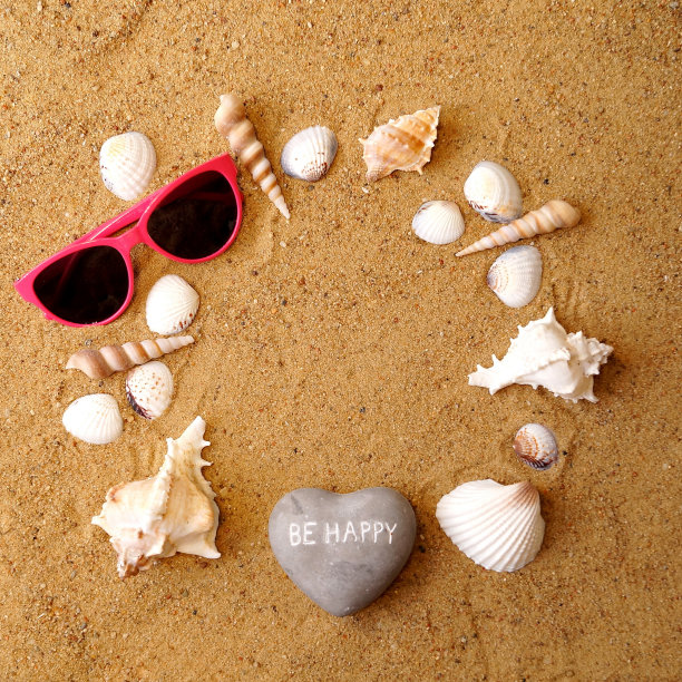 刻有“快乐吧”字样的心形石头、玻璃和各种贝壳呈圆形摆放在沙滩上。在中间有一个地方可以放你的笔记——copyspace图片下载