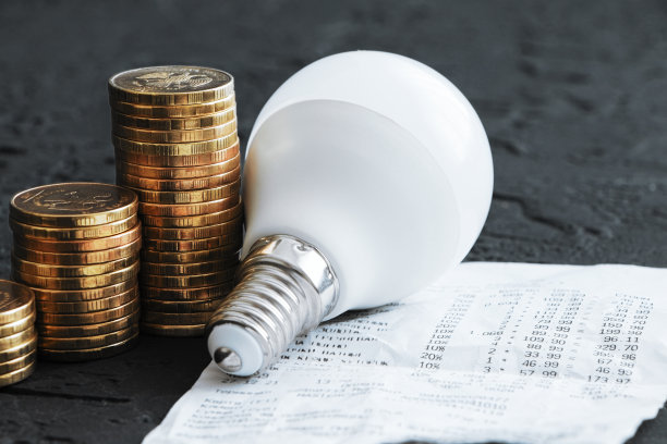 电费。节能。节能灯泡。硬币在黑暗的背景上。节能。堆栈的硬币图片下载