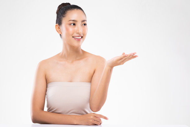 美丽迷人、富有魅力的亚洲年轻女性，笑容灿烂，露出洁白的牙齿，张开手掌展示化妆品，拥有健康的肌肤，美容化妆品概念素材图片