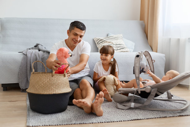 照片中，黑发男子身穿白色休闲风格t恤和牛仔裤短裤坐在地板上，父亲与孩子和玩具玩耍，表达着幸福。图片下载