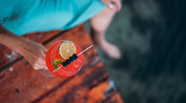 一个女人的手握着一杯红色的鸡尾酒，站在木制的码头上图片下载