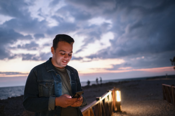 一个微笑的年轻人的肖像使用智能手机看着智能手机的屏幕图片下载