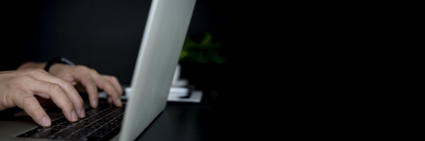 一名男子在办公室的办公桌前，使用笔记本电脑研究新项目的创意，直到深夜图片下载