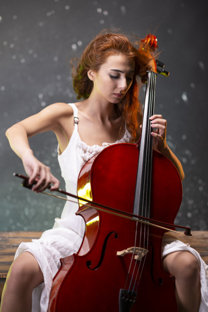红发白裙的女孩拉大提琴。图片下载