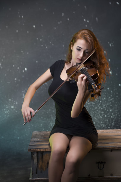 美丽的年轻女子在黑色背景下拉小提琴。图片下载