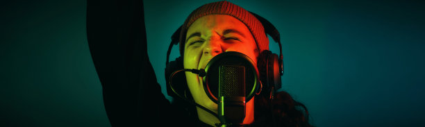 十几岁的女孩戴着一顶羊毛帽子，用麦克风和耳机唱歌，她的眼睛是闭着的，孤立在绿色的背景上，复制空间，极端近距离看图片下载