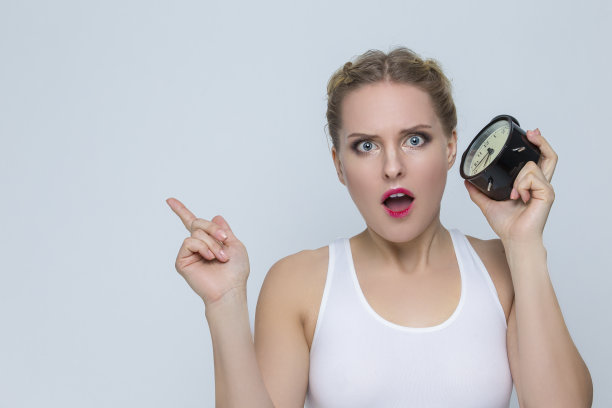 现代生活方式的概念。年轻紧张的白人女性用闹钟和举起手的手势。图片下载