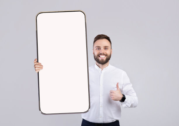 年轻快乐的男子拿着智能手机，屏幕是空白的，大拇指朝上图片下载