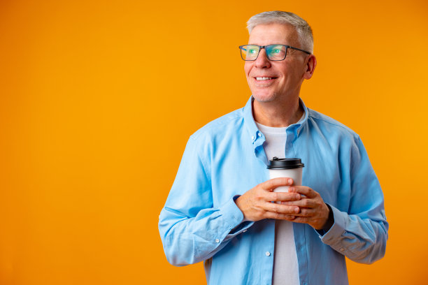 一位戴眼镜的英俊老人，黄色背景上拿着一杯咖啡图片下载