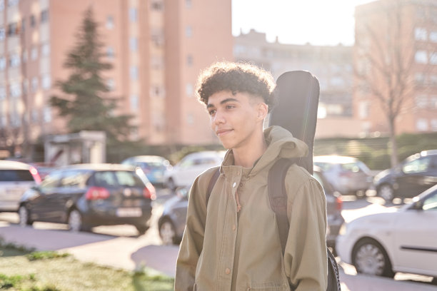 这是一幅年轻男子在户外摆姿势的肖像，他的吉他演奏包，模特是拉丁美洲民族。图片下载