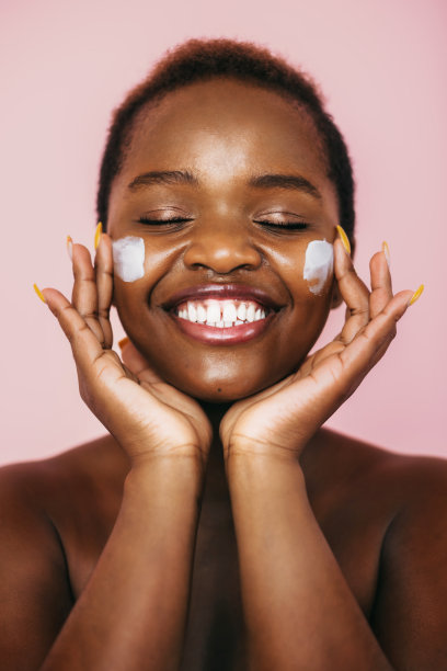 笑的女人用保湿霜在她的脸上孤立在粉红色的背景上。美容治疗。美丽的脸。图片下载