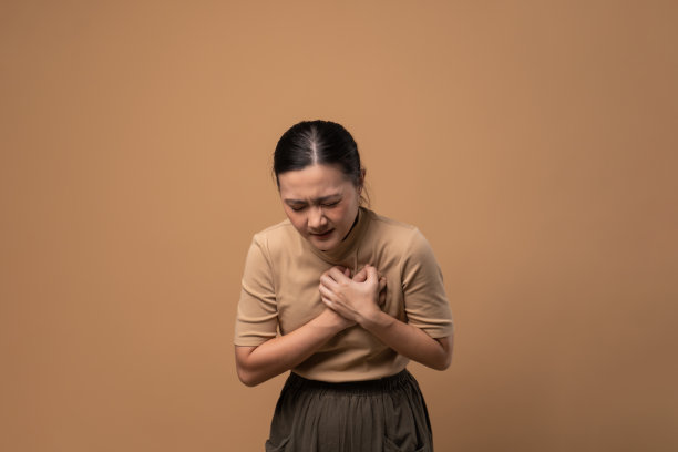 一名亚洲妇女患胸痛，背景为米色。图片下载