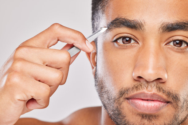 一个年轻人在灰色背景下拔眉毛的照片图片下载