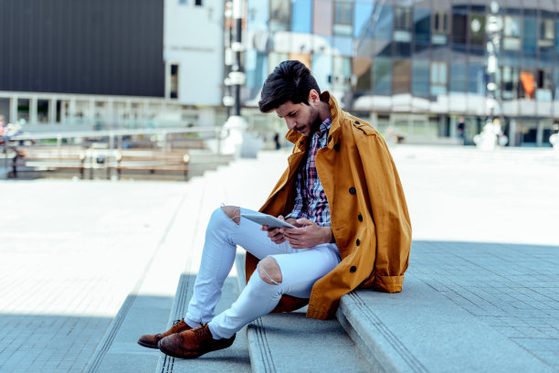 年轻人在城市广场坐着，看着平板电脑图片下载