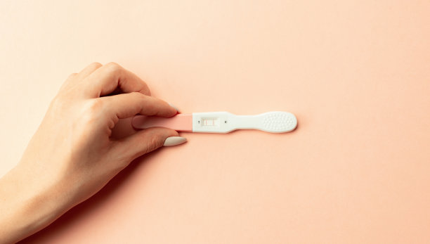 妊娠试验阳性。女性手握阳性怀孕测试与丝带粉红色背景。医疗保健妇科，孕产期产妇的观念。图片下载