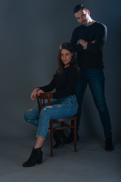 美丽的女人坐在椅子上，英俊的男人站在她旁边的黑暗背景的工作室图片下载