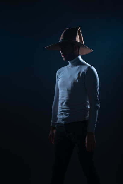 一个性感的年轻男子的肖像与牛仔帽摆姿势在高对比和黑暗的背景工作室图片下载