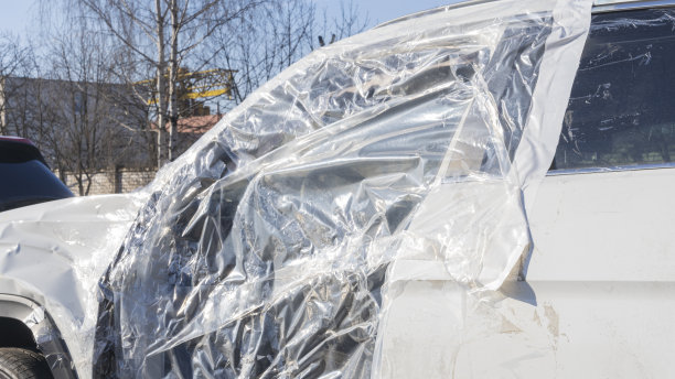 一辆白色的车出了车祸。运输车被撞凹了，门被损坏了。塑料薄膜将司机的车门关上。图片下载