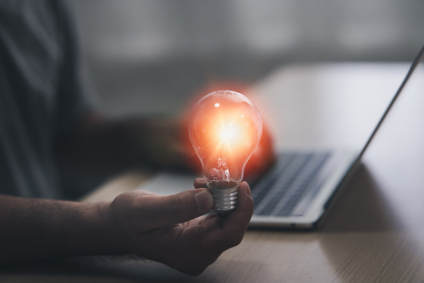 拿着灯泡的人手里面有个齿轮图标他在用笔记本电脑。来自在线技术的灵感。创新理念的概念。图片下载