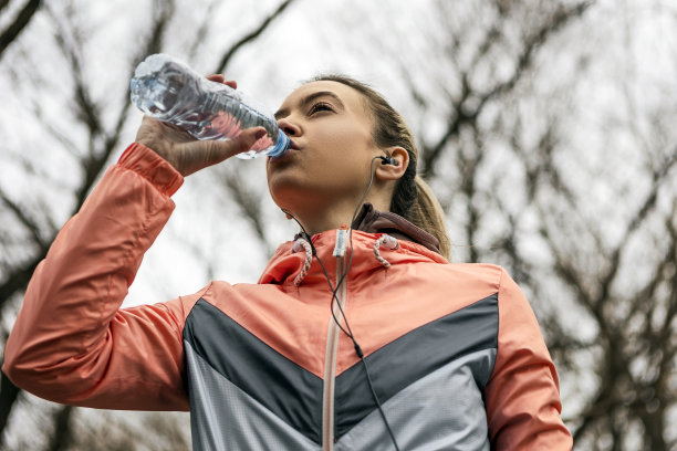 年轻女运动员在公园里戴着耳机喝水图片下载